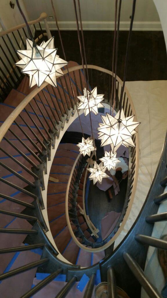 large spiral staircase with oak handrails and black balusters.  multiple star shaped lights hang in the center of the staircase.