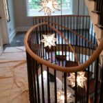 large spiral staircase with oak handrails and black balusters. multiple star shaped lights hang in the center of the staircase.