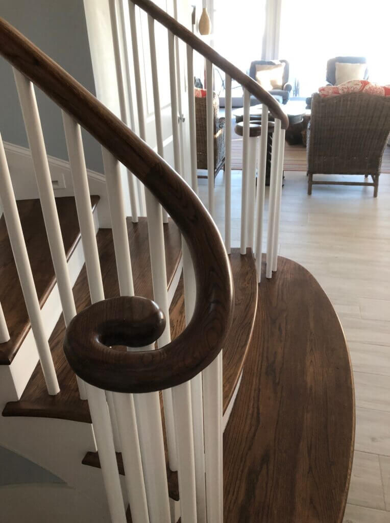 Close up of the base of a stained and painted wood staircase with a handrail that has a scrolled end