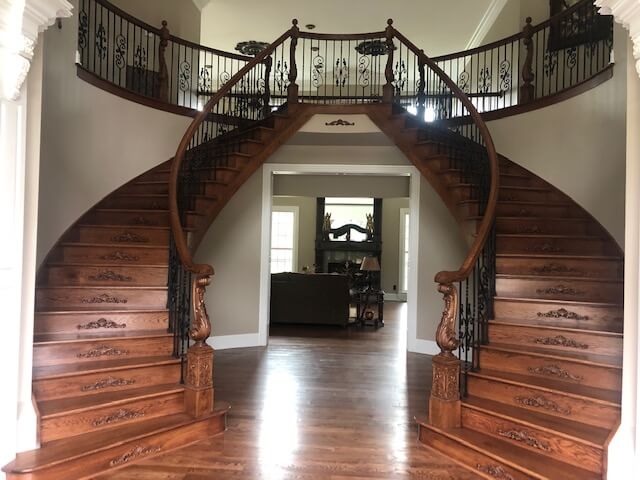 Entry of a home with a pair of matching curved ornate wooden staircases.