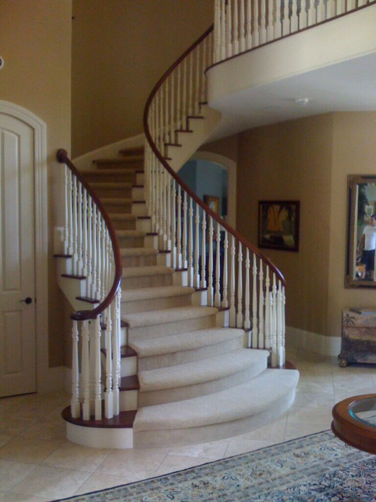 Staircase in the home with a flared bottom step. It has painted and stained wood parts