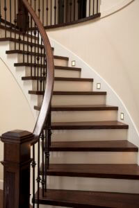 Curved wooden staircase with dark stained wooden treads and handrail and iron balusters